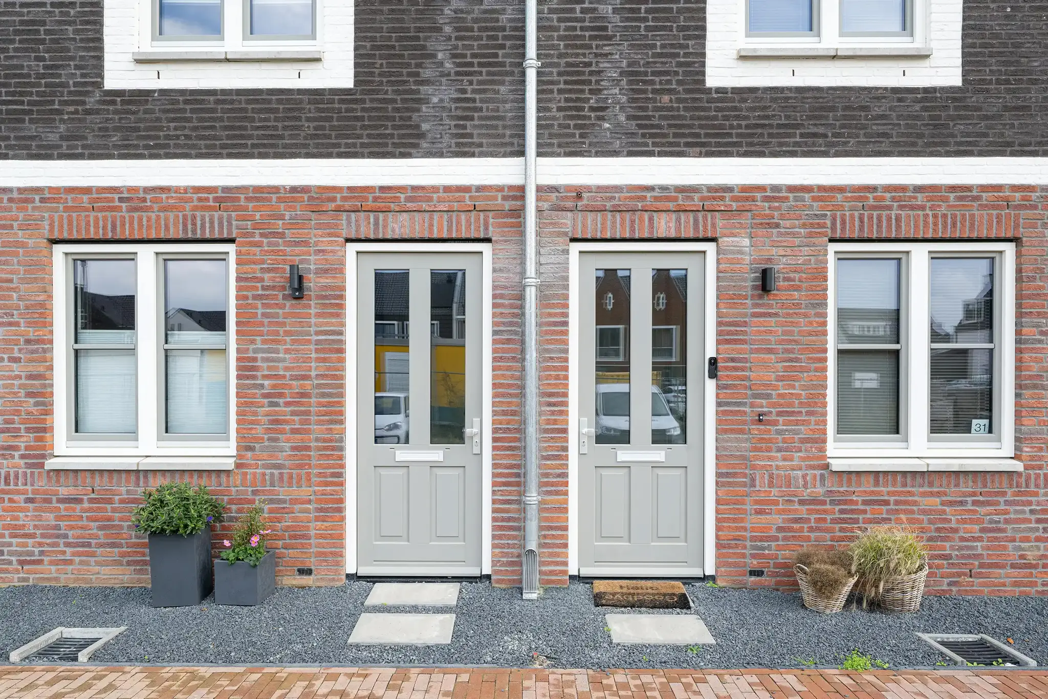 Twee lichtgrijze klassieke paneeldeuren met glas in een gevel van rode baksteen